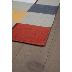 Dettaglio di un tappeto moderno con motivo geometrico in rosso, giallo, grigio e bianco.