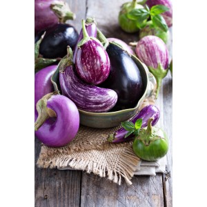 Melanzane di vari colori (t.b.t.) in una ciotola su un tavolo rustico di legno.