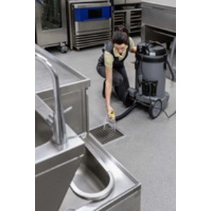 Donna pulisce scarico con aspiratore industriale t.b.t. in cucina in acciaio inox.