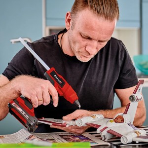 Uomo usa pistola per colla a caldo a batteria Einhell Power X-Change TE-CG 18 Li per lavori di bricolage. Pistola per colla a caldo rossa con batteria.