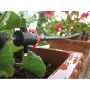 Sistema di microirrigazione in uso: tubo nero con valvola arancione che irriga una pianta in vaso.