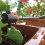 Sistema di microirrigazione in uso: tubo nero con valvola arancione che irriga una pianta in vaso.