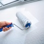 Rullo a dispersione LUX 18 cm mentre dipinge una parete. Rullo con manico blu e rivestimento grigio e bianco.