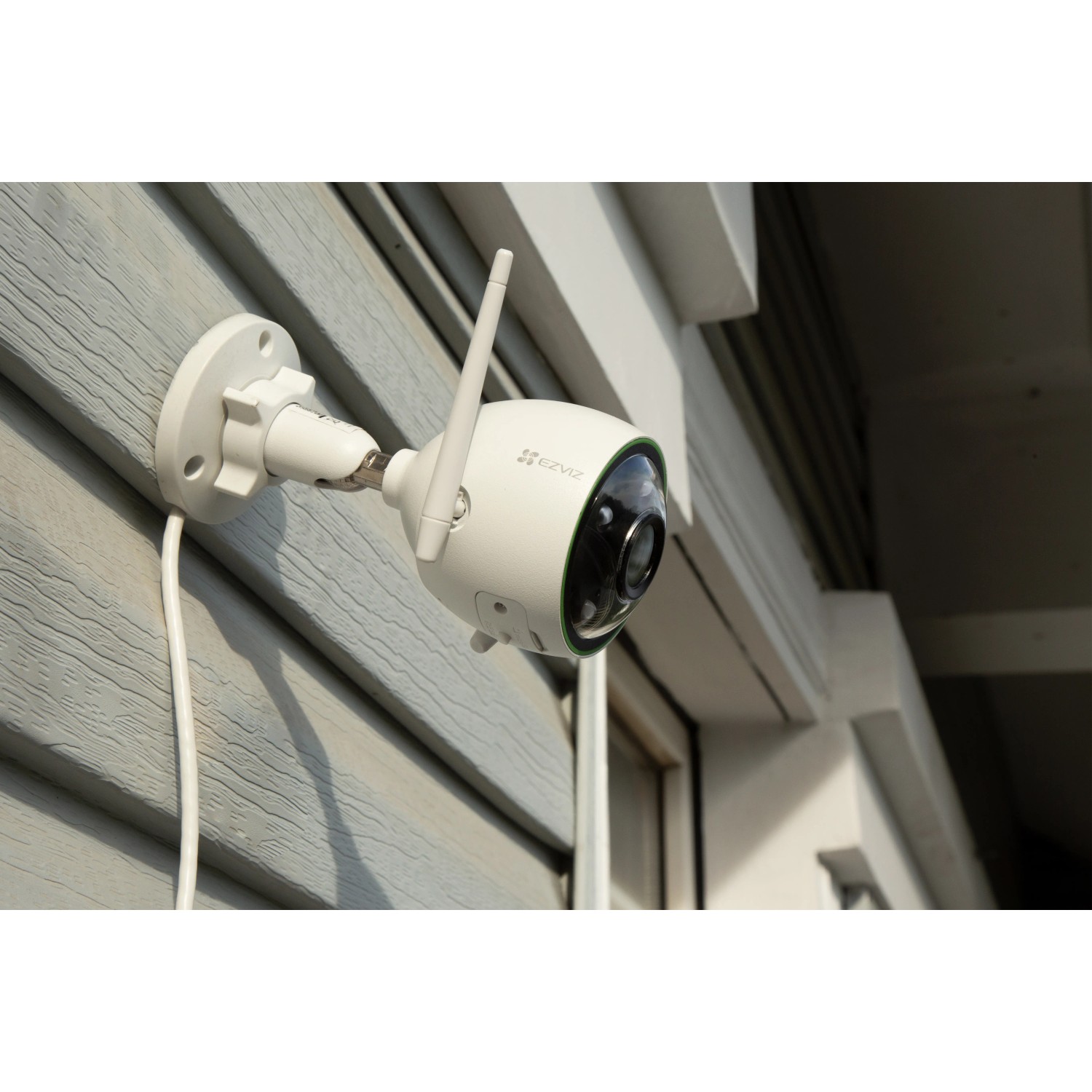 Telecamera di videosorveglianza bianca con antenna montata su una parete di casa.