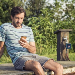 Uomo che utilizza il controllo dell'irrigazione Bluetooth Gardena tramite smartphone in giardino.