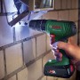 Avvitatore a percussione a batteria Bosch che fora un muro di mattoni, con batteria e luce LED.