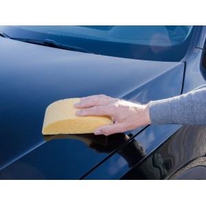 Mano che pulisce l'auto con spugna gialla CMI, forma semicircolare.