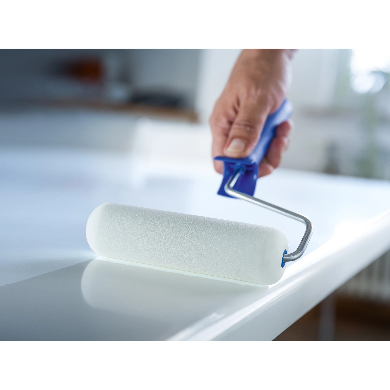 Rullo di schiuma LUX 16 cm bianco mentre vernicia una superficie liscia e bianca.