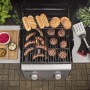Barbecue a gas con salsicce, hamburger, pane, insalata e utensili per barbecue sulla griglia.