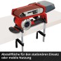 Levigatrice a nastro a batteria Einhell TP-BS 18/457 Li BL Solo con scatola raccoglipolvere e nastri abrasivi su banco.
