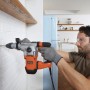Uomo che fora un muro con un martello perforatore Black+Decker BEHS03K. Trapano arancione/argento.