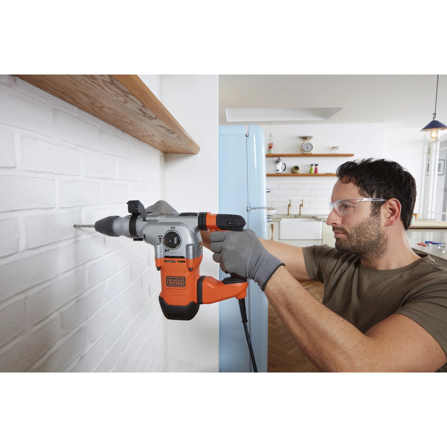 Uomo che fora un muro con un martello perforatore Black+Decker BEHS03K. Trapano arancione/argento.