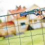 Pinza per recinzioni Rapid FP222 che fissa il filo a una recinzione da giardino verde.