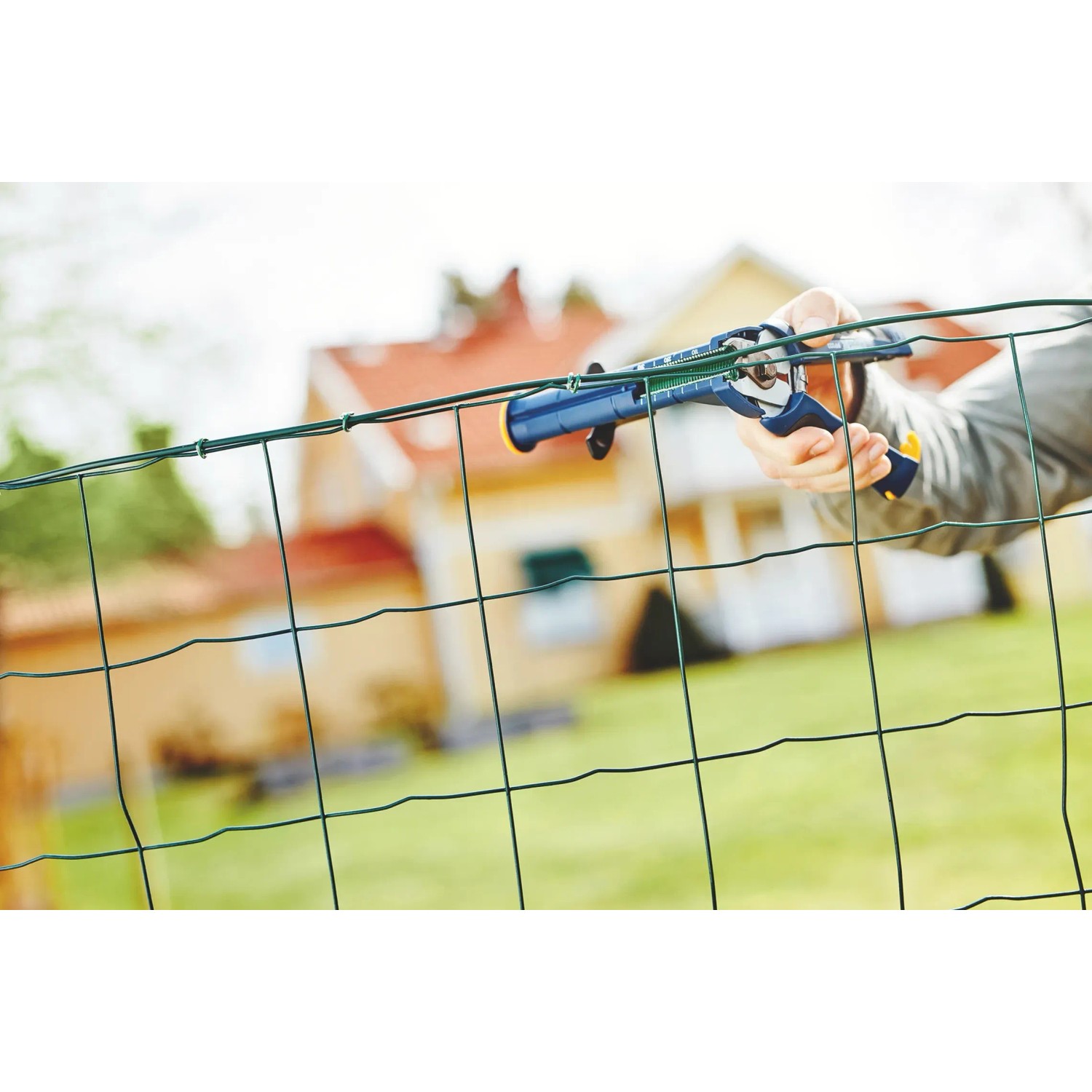 Pinza per recinzioni Rapid FP222 che fissa il filo a una recinzione da giardino verde.