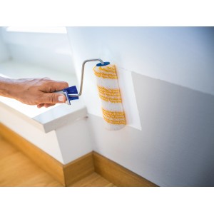 Rullo per dispersione LUX 15 cm mentre dipinge una parete. Rullo con strisce gialle e manico blu.