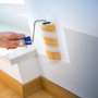 Rullo per dispersione LUX 15 cm mentre dipinge una parete. Rullo con strisce gialle e manico blu.