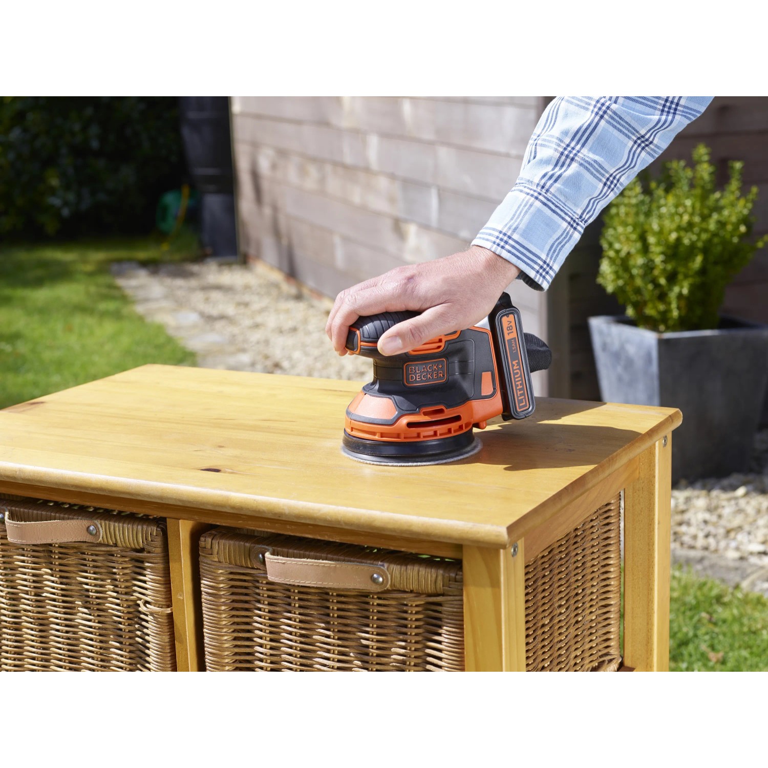 Levigatrice eccentrica a batteria Black+Decker BDCROS18N mentre leviga un comò di legno all'aperto.