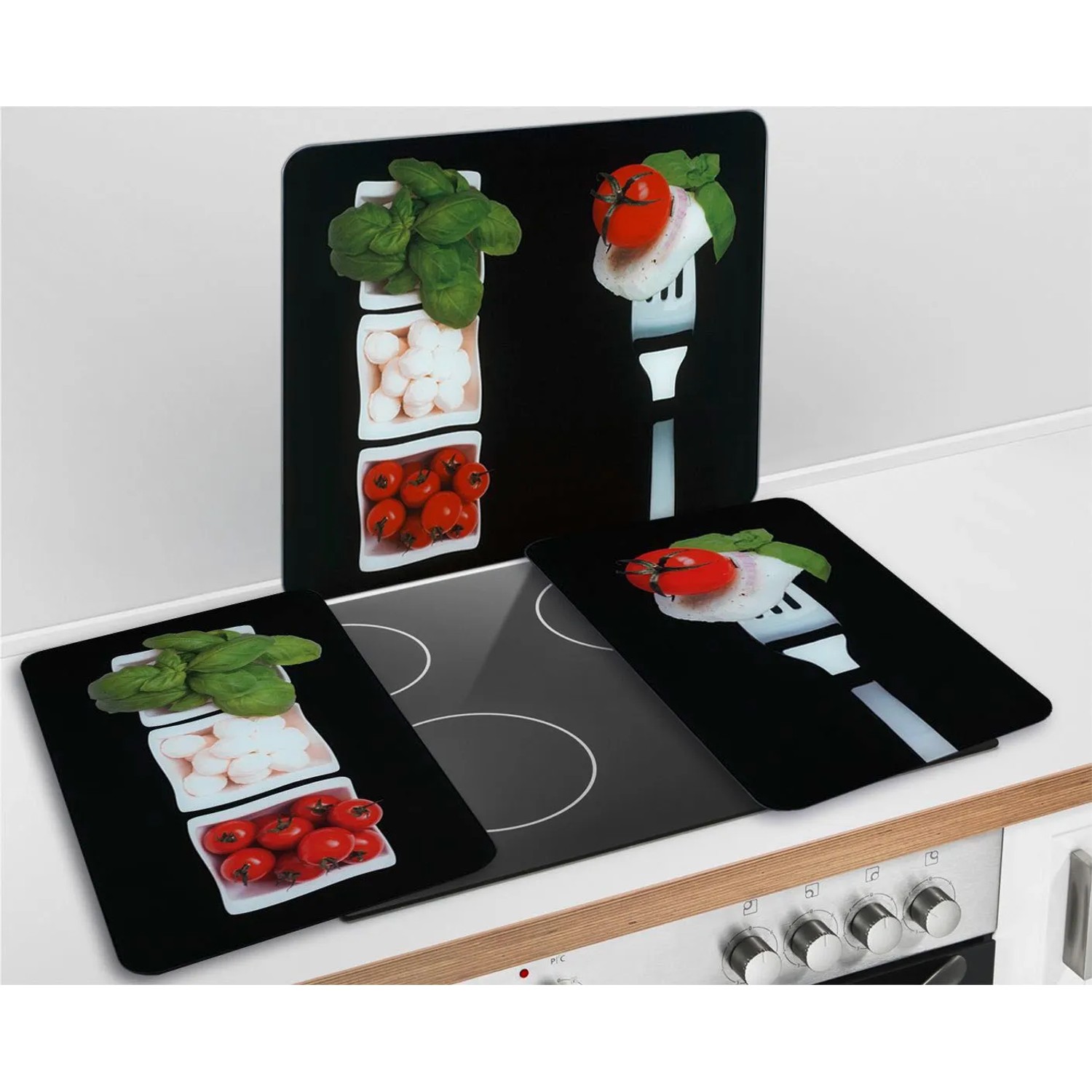 Set di 2 coperture per piano cottura Wenko Caprese con pomodori, mozzarella e basilico su sfondo nero.