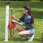 Donna con tubo per irrigazione t.b.t. rosso collegato a un punto acqua in giardino.