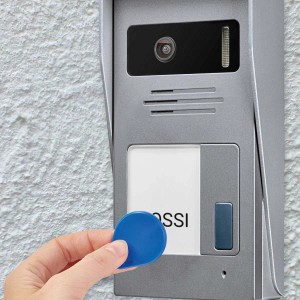 Citofono t.b.t. argentato con chip RFID in mano su muro bianco.