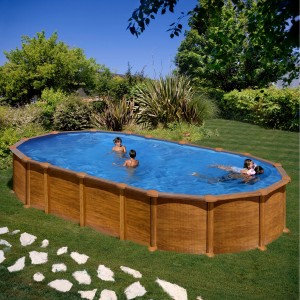 Piscina ovale Gre Amazonia effetto legno, piena d'acqua con persone che nuotano in giardino.