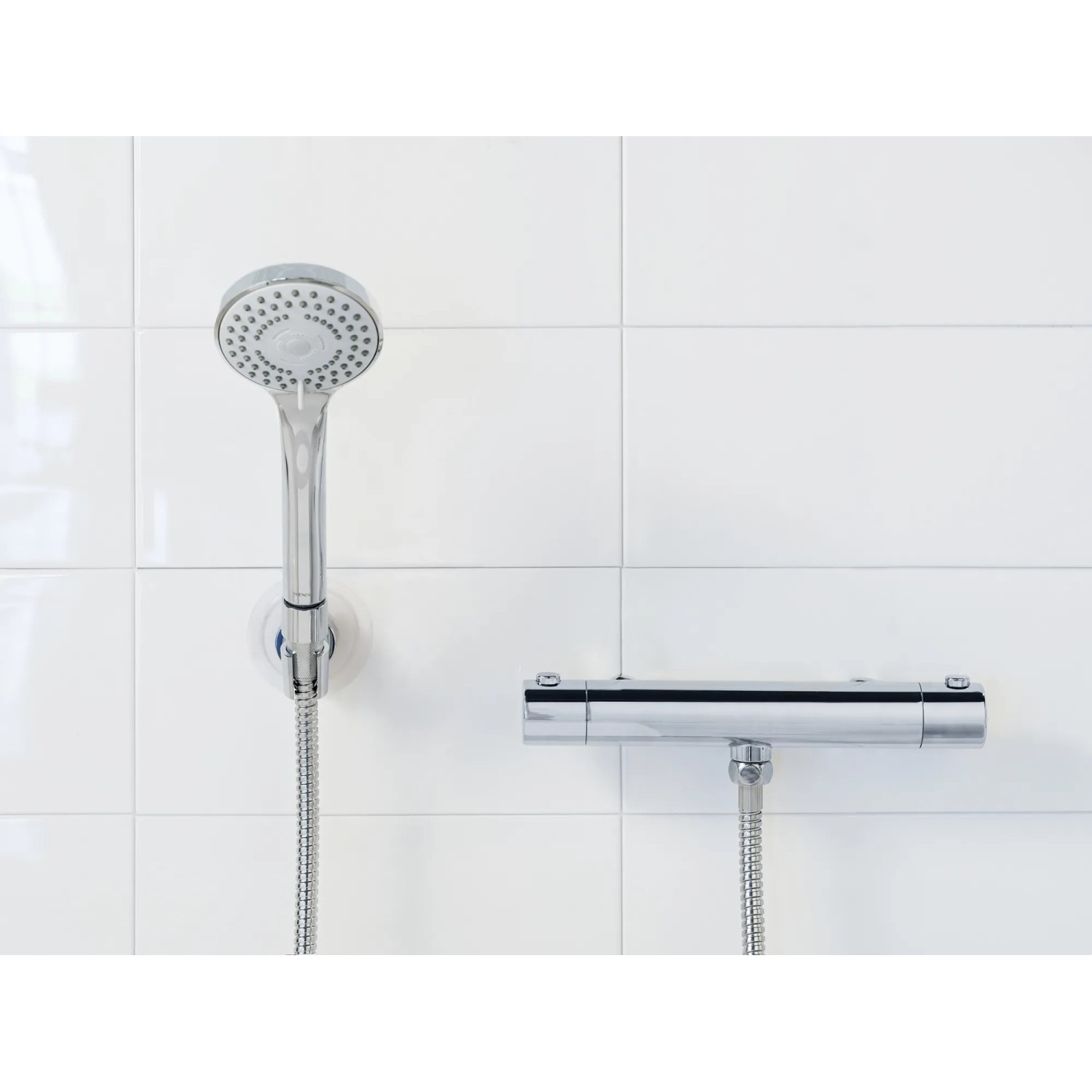 Set doccia Wenko Basic Line, 2 pezzi, soffione cromato con tubo flessibile su parete bianca.
