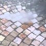 Mano che tiene la pistola per irrigazione t.b.t. che spruzza acqua su pavimento in pietra.