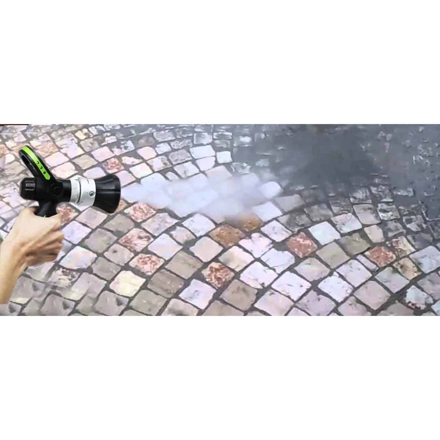 Mano che tiene la pistola per irrigazione t.b.t. che spruzza acqua su pavimento in pietra.