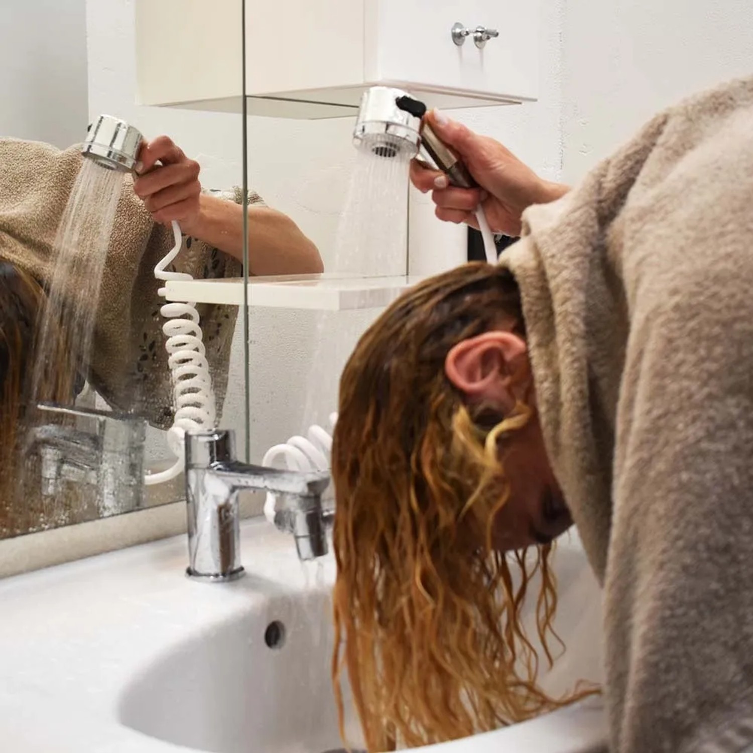 Donna che lava i capelli con doccetta t.b.t. al lavandino.
