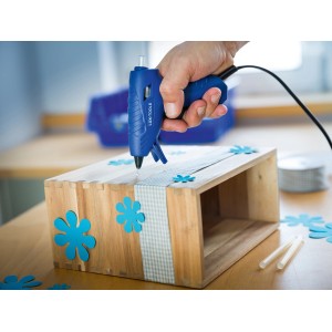 Pistola per colla a caldo LUX in uso per lavori di bricolage con legno e fiori decorativi blu.