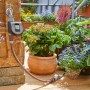 Computer per irrigazione Gardena Flex su rubinetto con piante sullo sfondo.