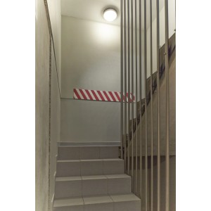 Vano scale con gradini grigi, ringhiera in metallo e segnaletica a strisce bianche e rosse.