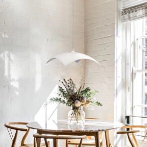 Lampada a sospensione bianca t.b.t. sopra tavolo da pranzo con vaso di fiori.