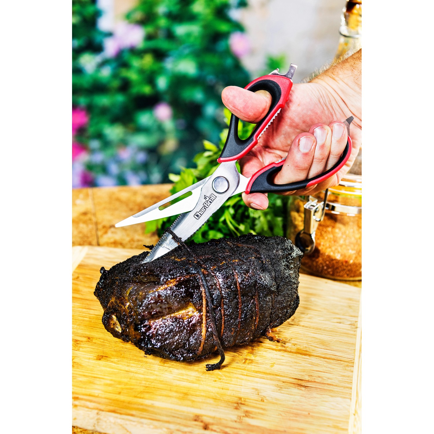 Forbici da carne Char-Broil tagliano arrosto su tagliere di legno. Utensile per grill con manici rossi.