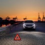 Auto con triangolo di emergenza e kit lampadine di ricambio Osram H4 sullo sfondo.