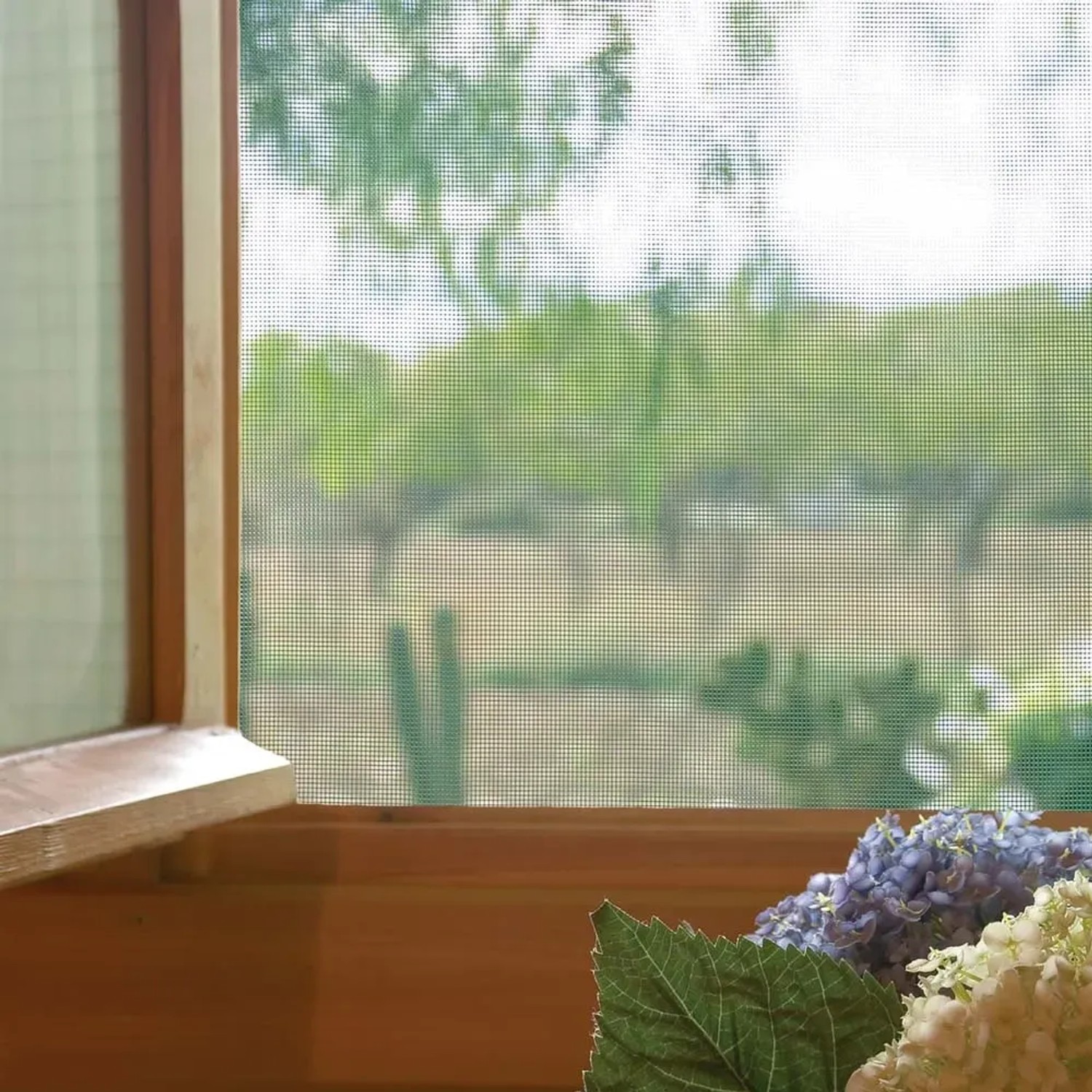 Finestra in legno con zanzariera e fiori in primo piano.
