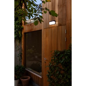 Lampada da parete solare a LED Lutec Fran nera e angolare su parete in legno. Luce esterna moderna con sensore di movimento.