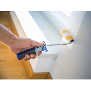 Mano che dipinge la parete con rullo a dispersione LUX 12 cm. Rullo con manico blu-grigio.