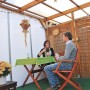 Terrazza coperta con pannelli in plastica trasparenti e persone rilassate al tavolo.