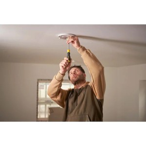 Un uomo sta avvitando qualcosa al soffitto con un cacciavite.