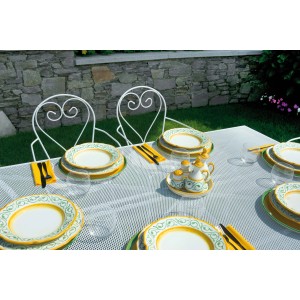 Tavolo da giardino apparecchiato con set di stoviglie. Piatti con decoro giallo-verde, bicchieri, posate e set di spezie.