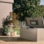 Biohort StyleBox 140 grigio quarzo metallizzato, coperchio aperto con molla a gas, su terrazza in legno. Box universale impermeabile.