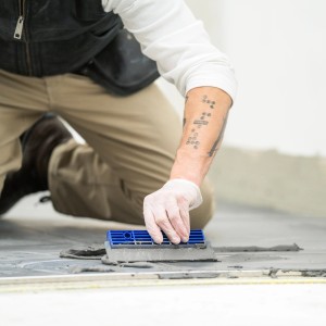 Artigiano che stende l'adesivo per piastrelle Mapei C2TE sul pavimento con una spatola dentata.