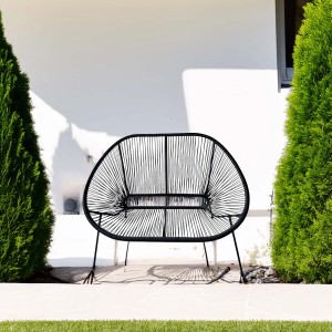 Divano da esterno/panchina da giardino t.b.t. nero in plastica intrecciata davanti a muro bianco.