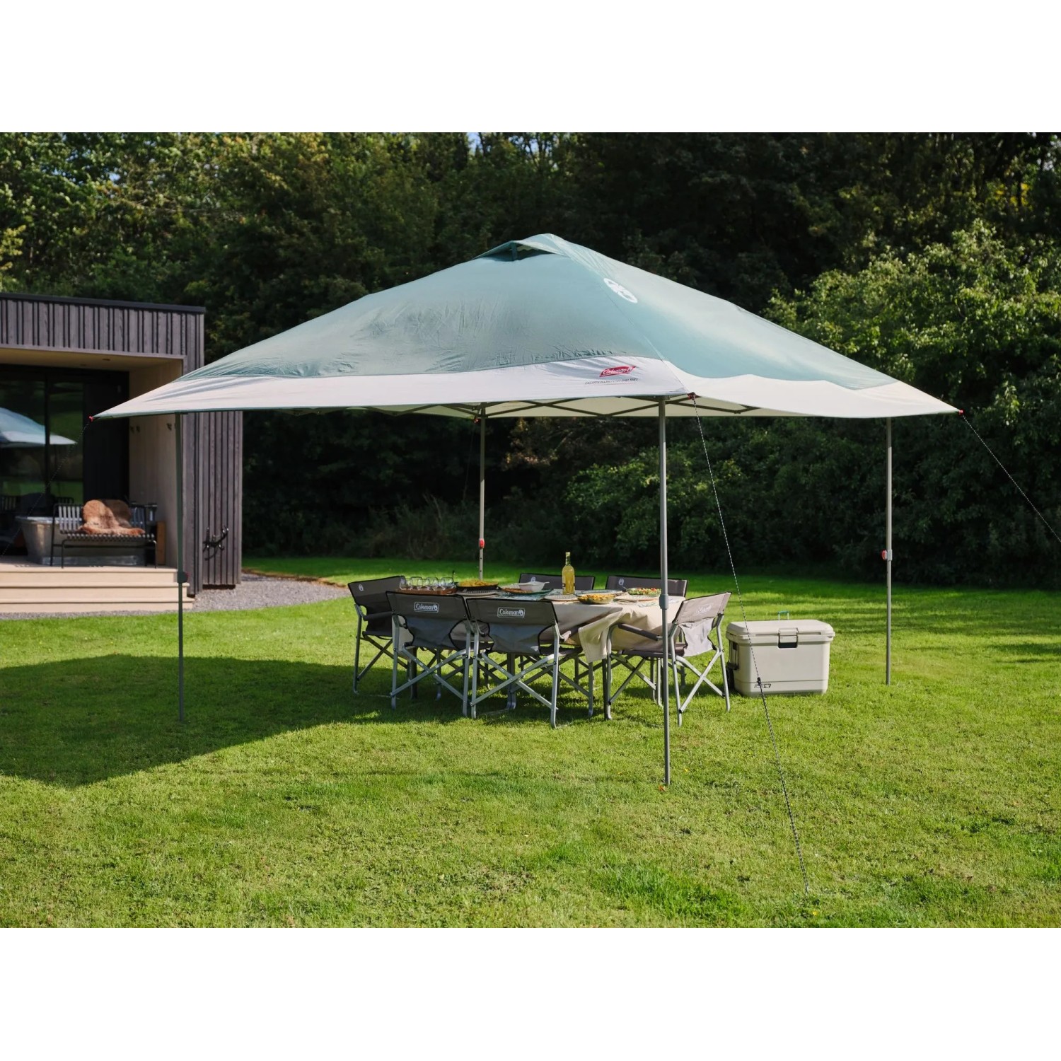 Tenda da campeggio Coleman FastPitch OnePush Shelter L verde e bianca con tavolo e sedie in giardino.