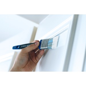 Mano che dipinge una porta bianca con un pennello piatto LUX da 30 mm. Pennello universale con impugnatura morbida.