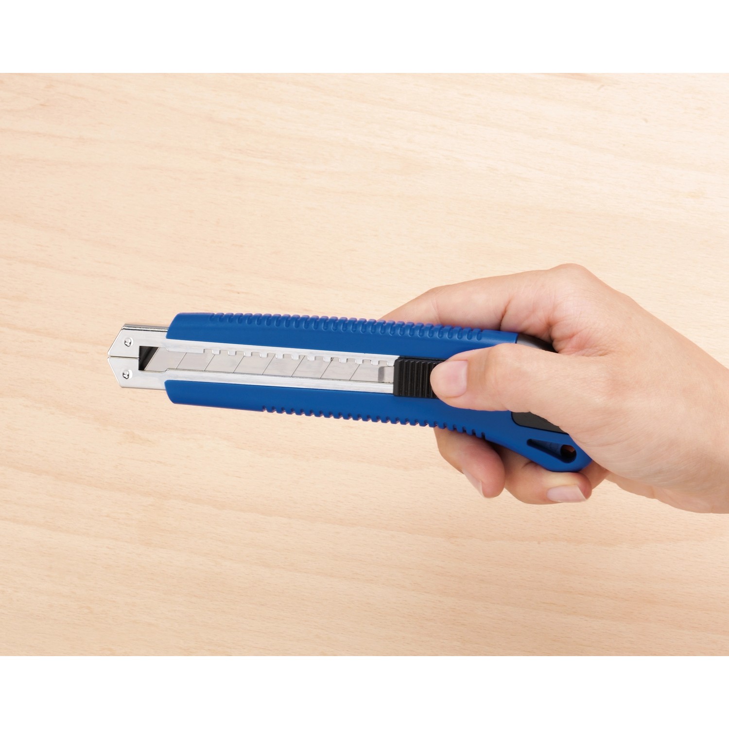 Mano che tiene un cutter LUX Classic 100 mm blu su sfondo di legno chiaro.