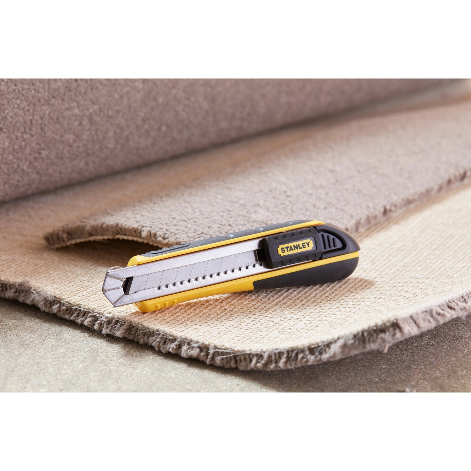 Cutter Stanley FatMax 18mm, nero-giallo, con lame a segmenti su tappeto.