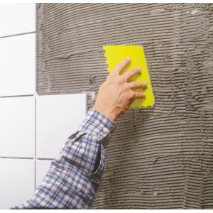 Spatola gialla LUX Spachtelsatz Classic che applica adesivo su una parete piastrellata.