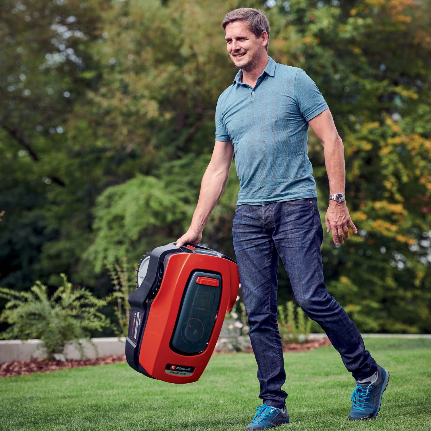 Uomo trasporta un robot tagliaerba t.b.t. rosso su un prato.